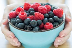 bowl of raspberries and blueberries held up by a person